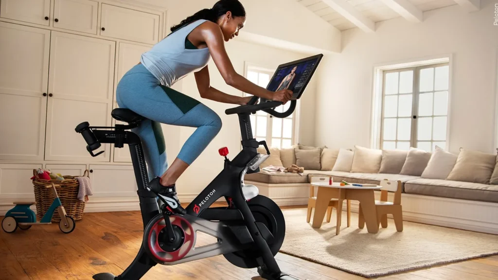 A woman rides a Peloton Bike+ during an online training session, symbolizing the Peloton recalls 833000 Bike units due to reported seat post failures.