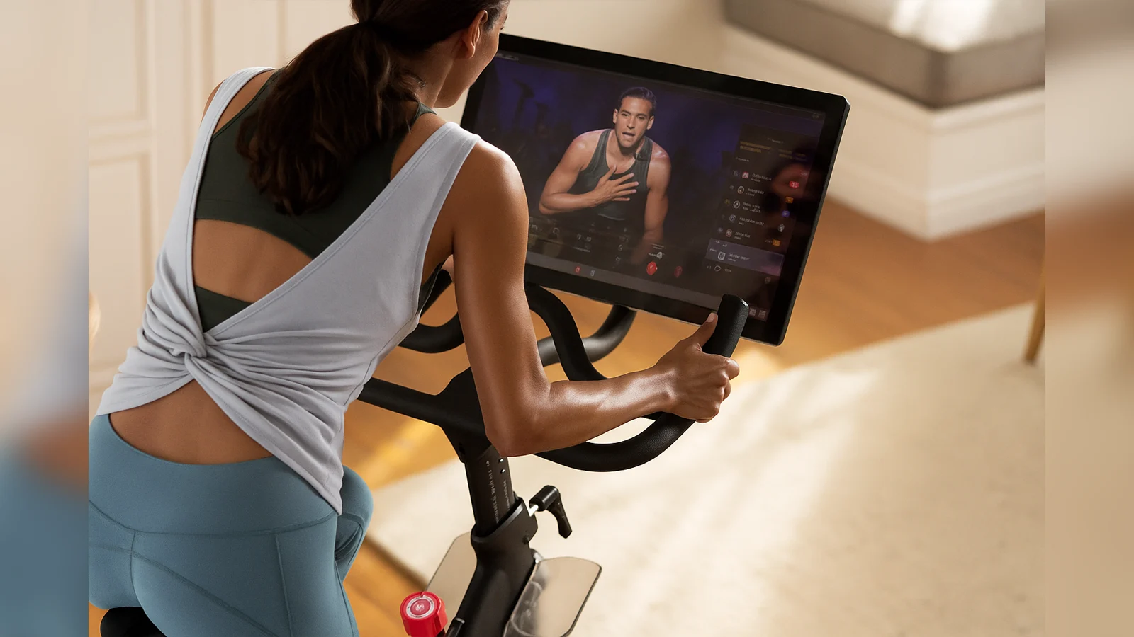 A woman using a Peloton Bike+ at home during a virtual fitness session, representing the Peloton recalls 2025 after safety concerns over seat post issues.