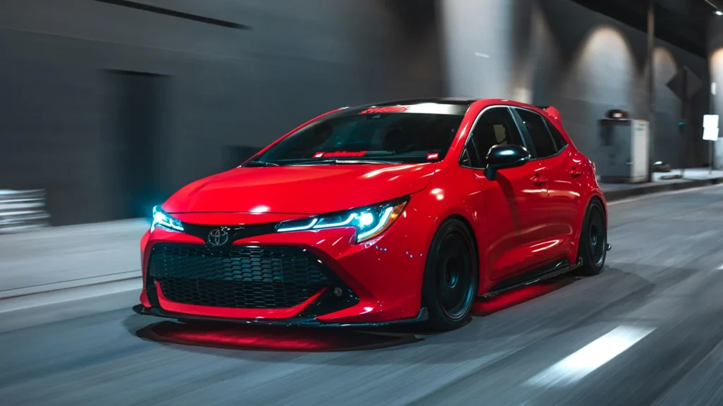 Rear three-quarter view of the 2025 Toyota Corolla hybrid EV showcasing its aerodynamic shape, LED tail lamps, and electric charging port illuminated under studio lighting.